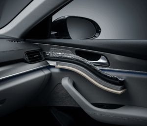 Interior mobil mewah yang tenang dan nyaman, dengan lapisan jenis peredam mobil terbaik yang terlihat sebagian pada panel pintu, menampilkan tekstur karet, foil, dan serat yang berbeda. Pencahayaan studio yang realistis dan detail tinggi menciptakan suasana yang tenang dan mewah.