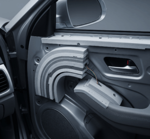 Pemandangan detail dari sudut pandang tinggi di dalam kabin mobil, menampilkan peredam busa mobil yang sebagian telah terpasang pada panel pintu mobil. Terlihat berbagai lapisan busa, beberapa kabel, dan struktur logam pintu mobil. Suasana yang tenang dan hening, dengan cahaya lembut yang menyoroti efektivitas peredam suara. Gaya modern dan bersih, dengan pencahayaan realistis.