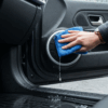 Tangan dengan jam tangan mengeringkan speaker mobil kena air, tetesan air terlihat jelas, pintu mobil terbuka.