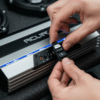 Tangan sedang menyesuaikan sakelar fase pada amplifier audio mobil yang ramping dan modern.